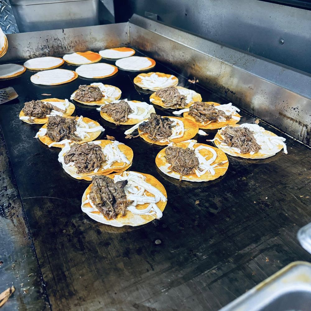 Tortillas layered with cheese and slow-cooked beef crisping up on the flat-top griddle inside the truck.
