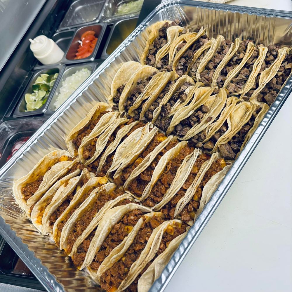 A large tray packed with tacos in soft corn tortillas, filled with asada, chorizo and al pastor.