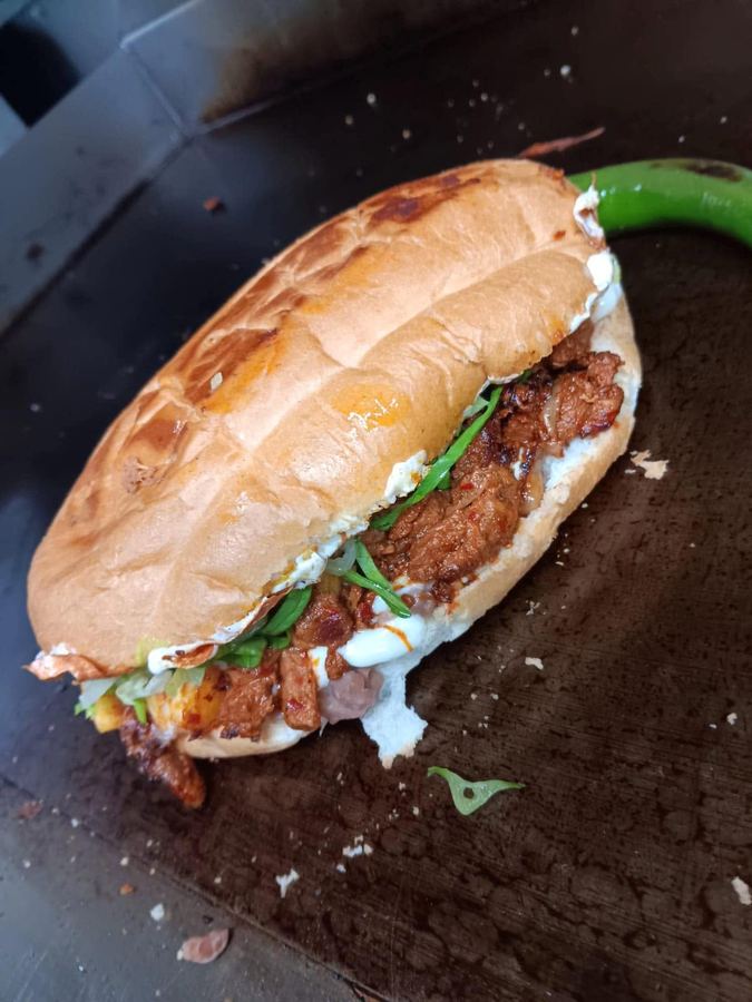 A torta on a toasted roll stacked with marinated meat, beans, crema and lettuce.