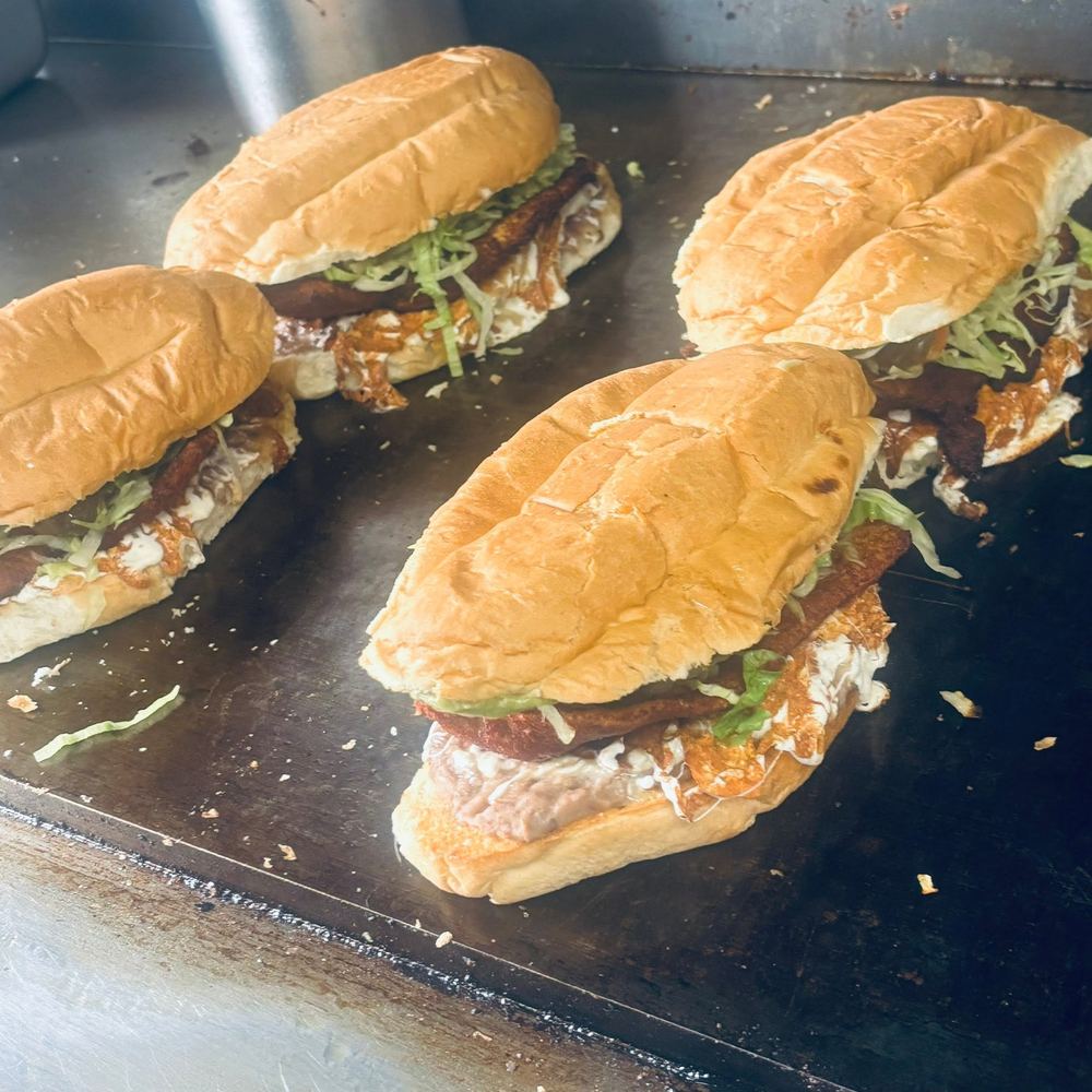 Four tortas toasting on the griddle, layered with beans, crema, lettuce and crispy meat.