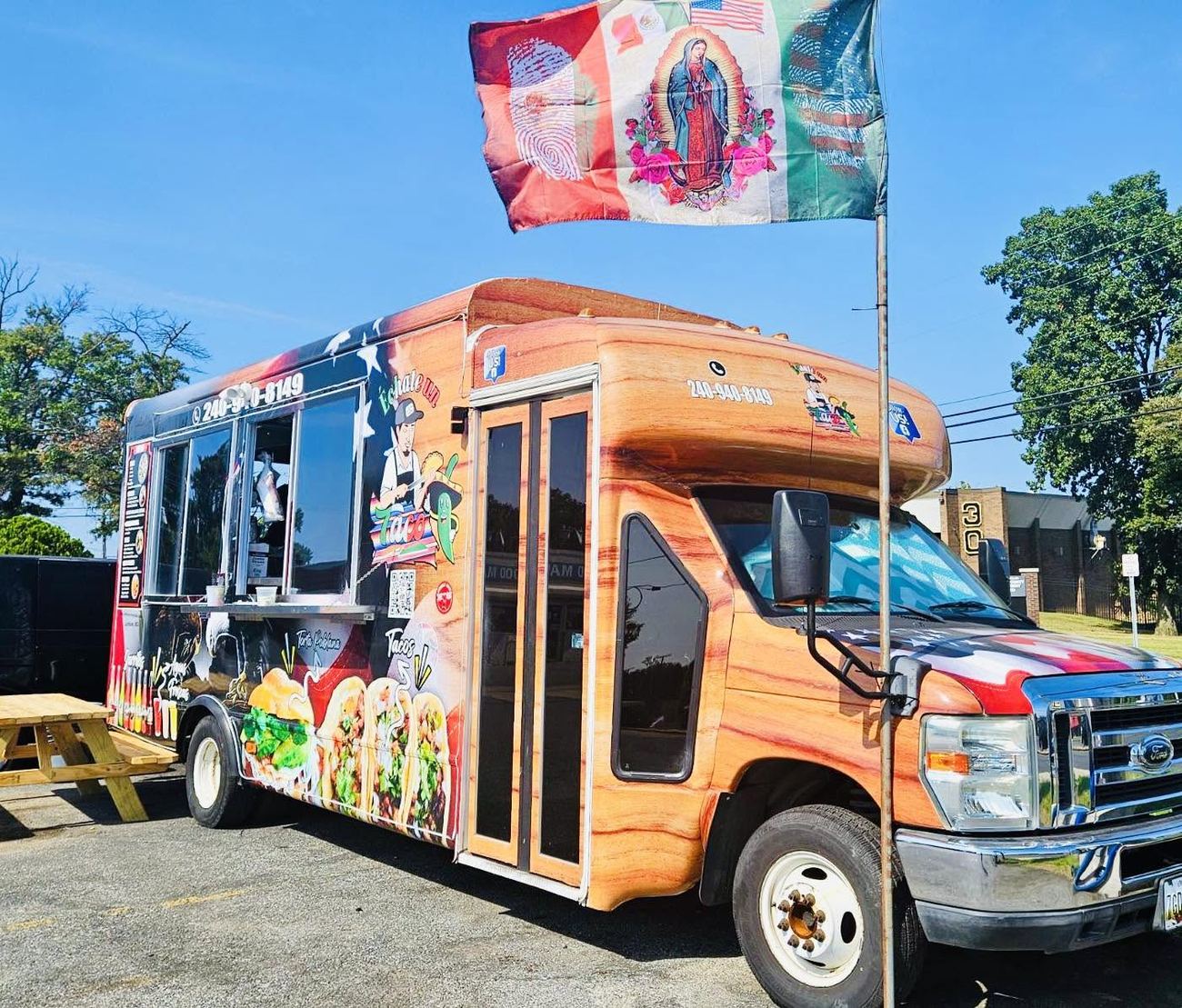 The Échate un Taco food truck parked on a sunny day, wrapped in artwork of tacos and tortas with the logo on the side and a flag flying above.